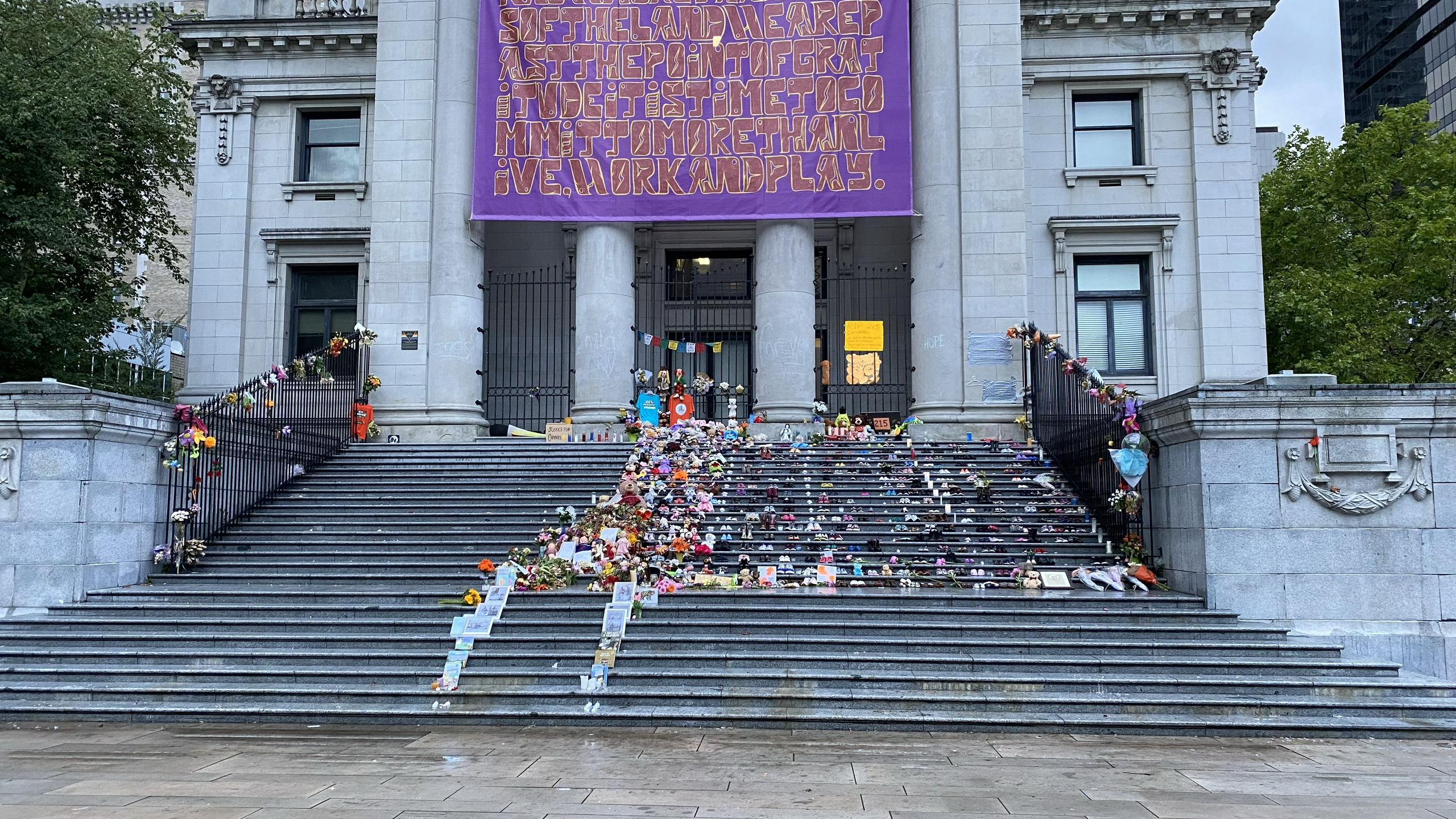 The staircase leading up to the pillared doors of the Vancouver Art Gallery in British Columbia, Canada, strewn with teddy bears, books, images, flowers, and 215 pairs of children’s shoes as a community memorial to the 215 buried children discovered at Kamloops Residential School.